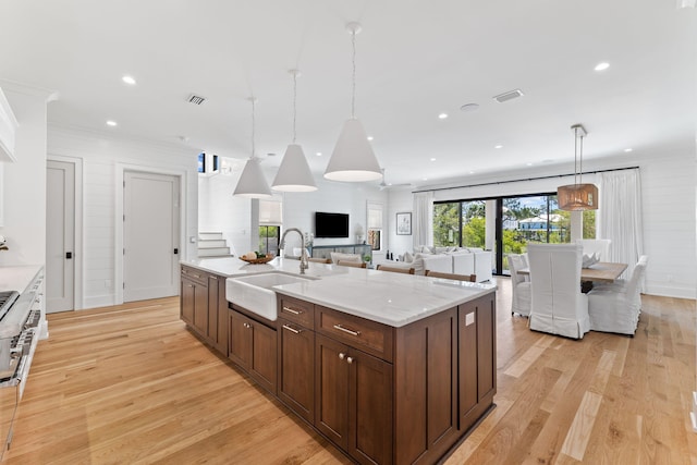 kitchen with light wood-type flooring, a center island with sink, sink, and decorative light fixtures