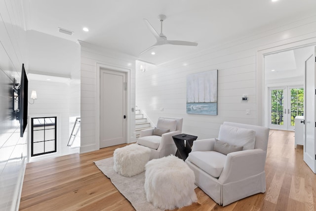 living area with wood walls, ceiling fan, light hardwood / wood-style flooring, and french doors