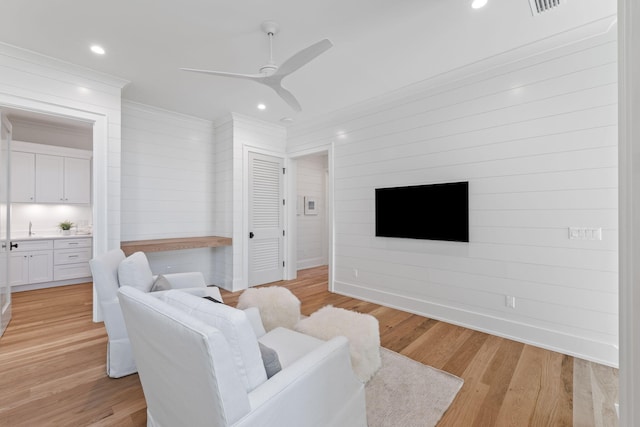 living room with wood walls, light wood-type flooring, sink, and ceiling fan