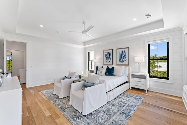 bedroom featuring light hardwood / wood-style flooring, ceiling fan, and a raised ceiling