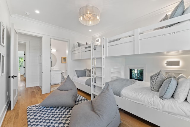 bedroom featuring ensuite bathroom, multiple windows, ornamental molding, and light hardwood / wood-style flooring