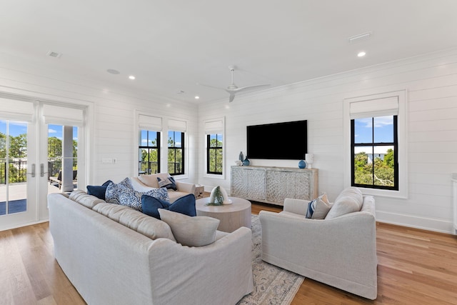 living room featuring wood walls, light wood-type flooring, ceiling fan, and a healthy amount of sunlight