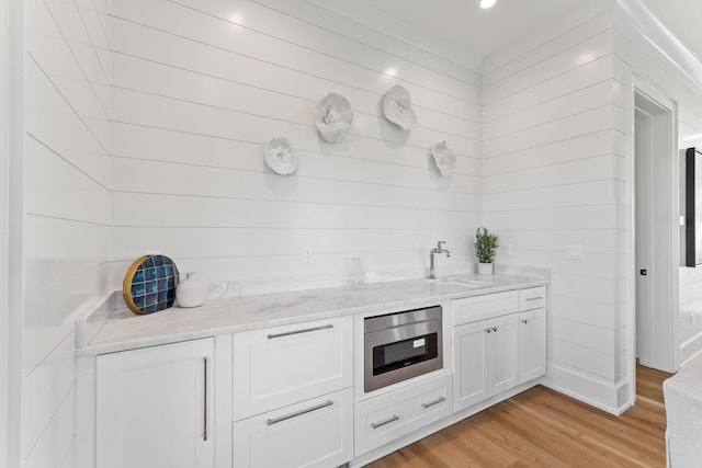 kitchen with white cabinetry, sink, light stone counters, light hardwood / wood-style flooring, and stainless steel microwave