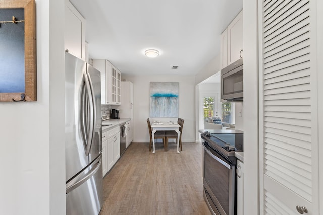 kitchen featuring hardwood / wood-style floors, white cabinetry, decorative backsplash, and appliances with stainless steel finishes