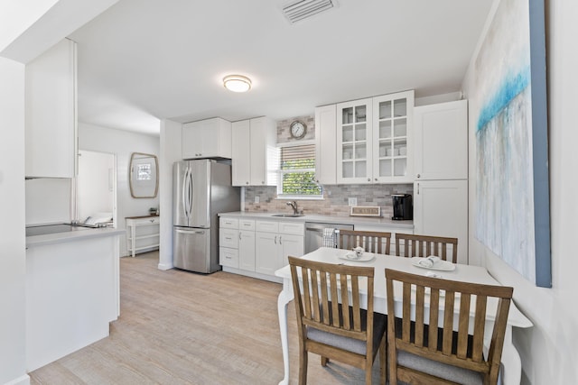 kitchen featuring stainless steel appliances, white cabinetry, sink, tasteful backsplash, and light hardwood / wood-style flooring