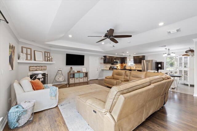 living room with a raised ceiling, ornamental molding, ceiling fan with notable chandelier, and dark hardwood / wood-style flooring