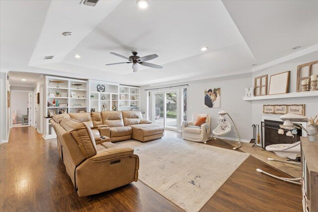 living room with a raised ceiling, wood-type flooring, ornamental molding, and ceiling fan