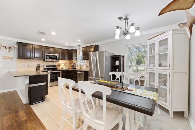 kitchen featuring crown molding, appliances with stainless steel finishes, pendant lighting, light stone countertops, and decorative backsplash