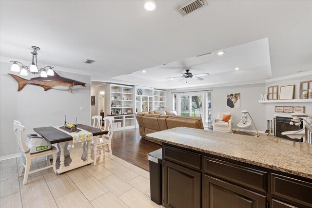 kitchen featuring pendant lighting, dark brown cabinets, light hardwood / wood-style floors, ceiling fan with notable chandelier, and a raised ceiling