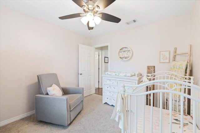 bedroom featuring light carpet, a nursery area, and ceiling fan