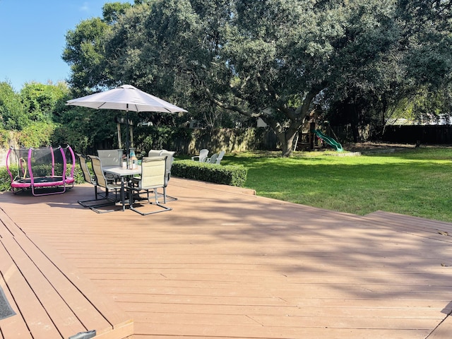 wooden deck with a playground, a trampoline, and a lawn