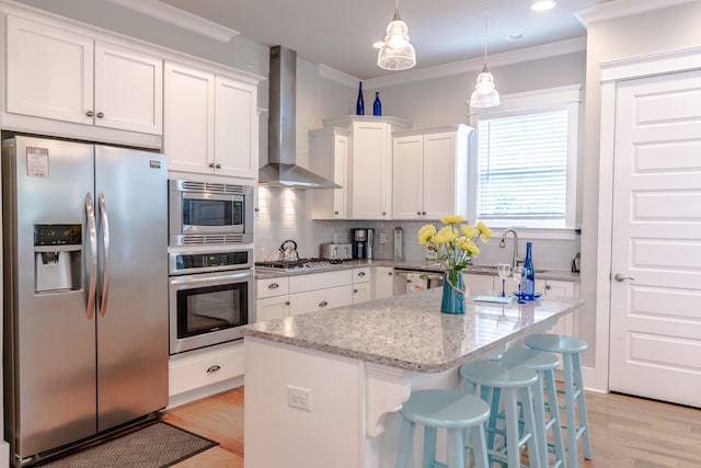 kitchen with wall chimney exhaust hood, stainless steel appliances, crown molding, pendant lighting, and white cabinets