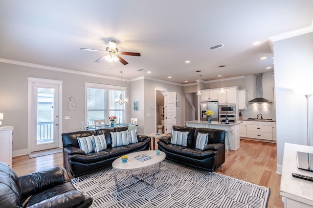 living room featuring ceiling fan with notable chandelier, light wood-type flooring, and crown molding