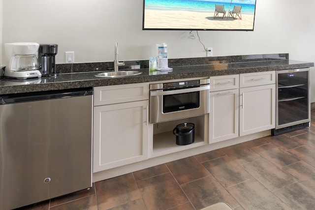 kitchen with beverage cooler, appliances with stainless steel finishes, sink, and white cabinets