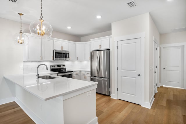 kitchen with kitchen peninsula, appliances with stainless steel finishes, sink, decorative light fixtures, and white cabinetry