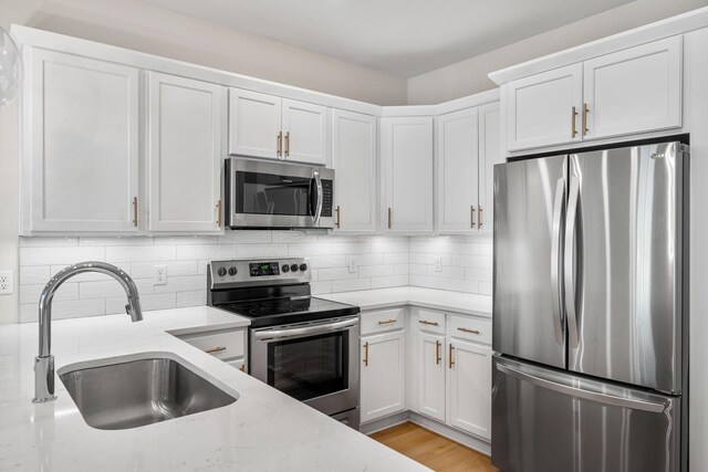22958 Ann Miller Rd, Panama City Beach, FL 32413 - kitchen with stainless steel appliances, white cabinetry, light stone counters, decorative backsplash, and light wood finished floors