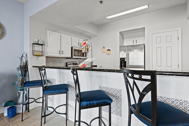 kitchen with a kitchen bar, stainless steel appliances, light tile patterned floors, tasteful backsplash, and white cabinetry