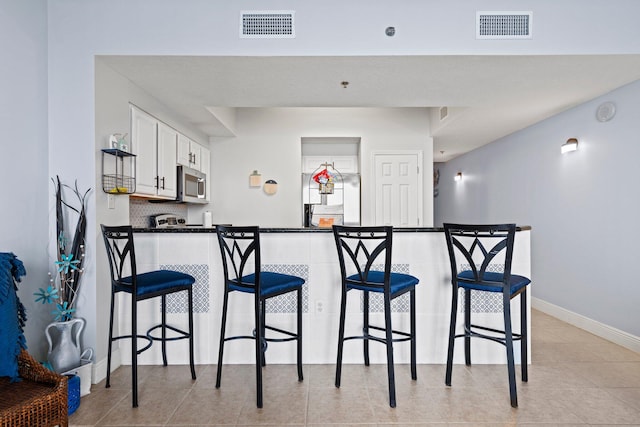 kitchen with white cabinetry, kitchen peninsula, appliances with stainless steel finishes, and a kitchen bar