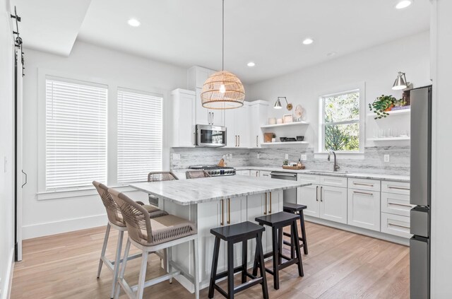 kitchen featuring light stone counters, appliances with stainless steel finishes, hanging light fixtures, sink, and white cabinets