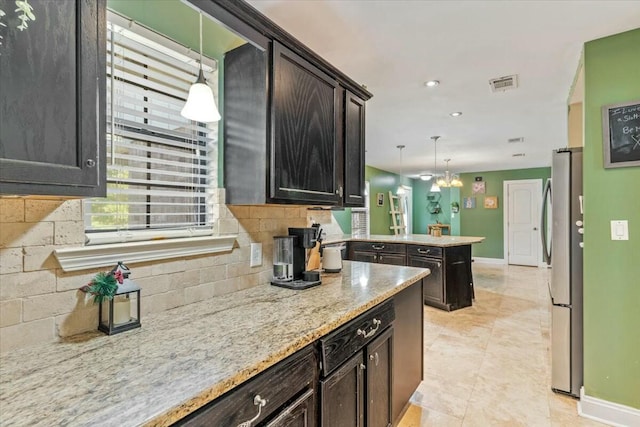 kitchen with stainless steel refrigerator, hanging light fixtures, tasteful backsplash, light stone counters, and kitchen peninsula