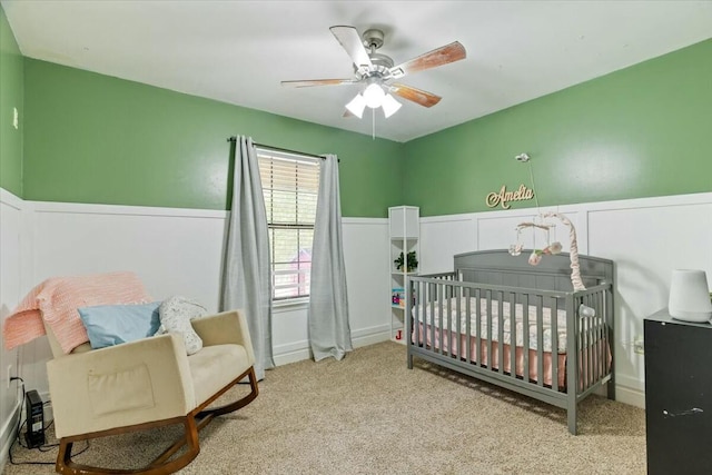 carpeted bedroom with a crib and ceiling fan