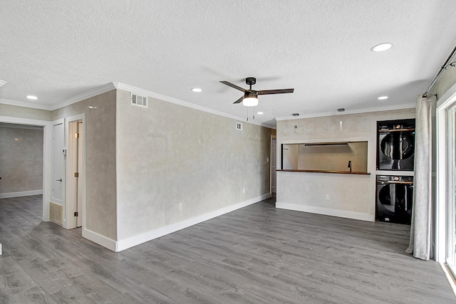 unfurnished living room featuring a textured ceiling, ceiling fan, stacked washer / drying machine, and hardwood / wood-style flooring