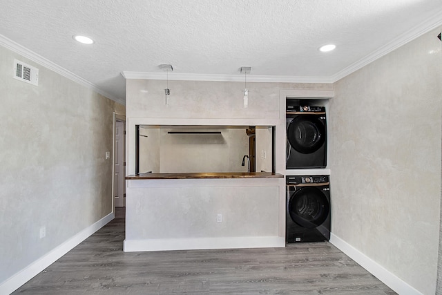 laundry room with a textured ceiling, stacked washer and dryer, hardwood / wood-style flooring, and crown molding