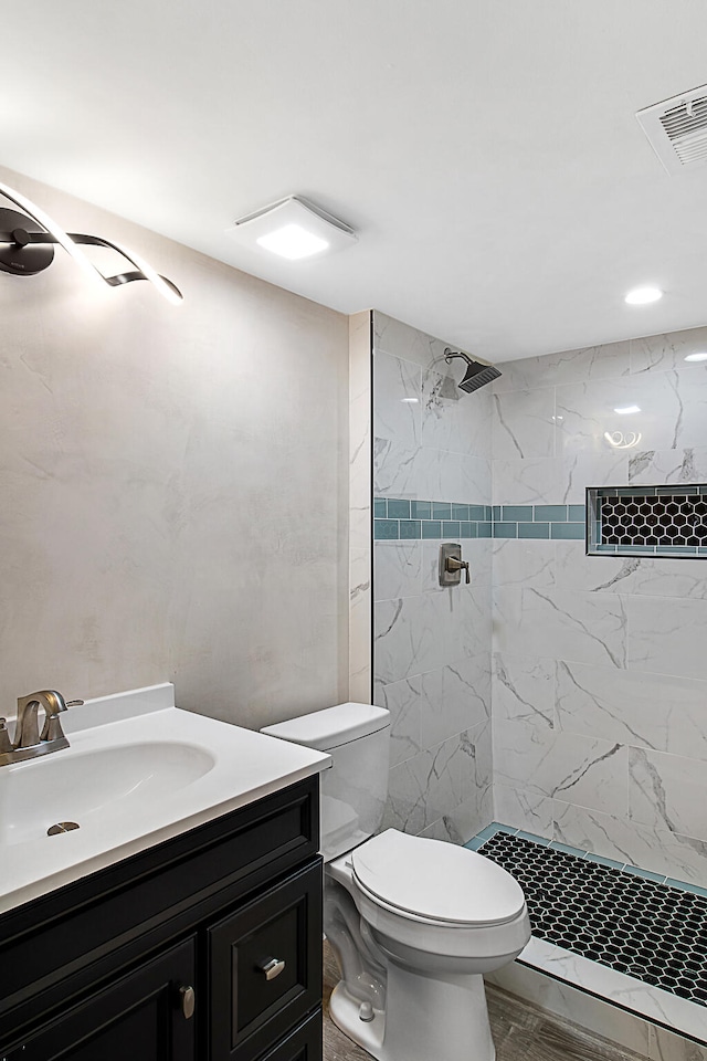 bathroom with hardwood / wood-style flooring, vanity, toilet, and tiled shower