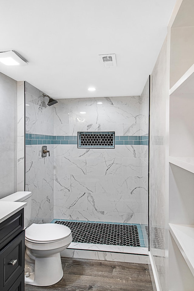 bathroom featuring a tile shower, toilet, vanity, and hardwood / wood-style flooring