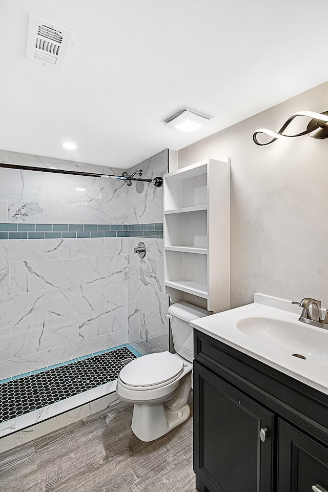 bathroom with hardwood / wood-style flooring, vanity, toilet, and tiled shower