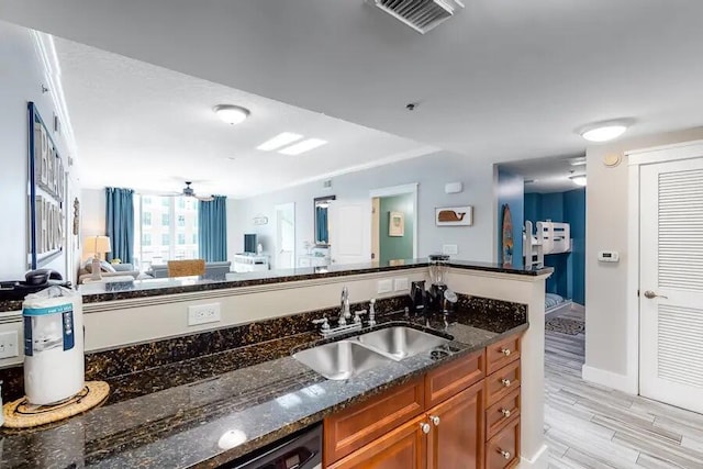 kitchen with a sink, brown cabinets, dark stone countertops, ceiling fan, and light wood-type flooring