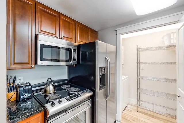 kitchen featuring appliances with stainless steel finishes, light wood-type flooring, brown cabinets, and dark stone counters