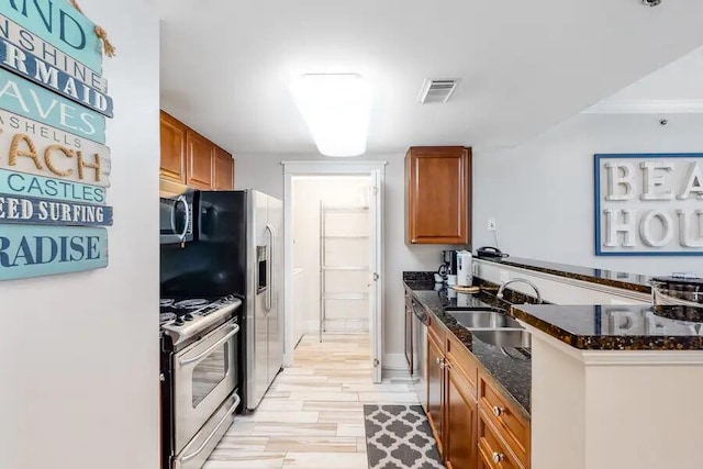 kitchen with light hardwood / wood-style floors, sink, kitchen peninsula, appliances with stainless steel finishes, and dark stone counters