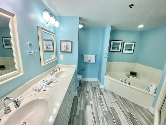 bathroom featuring toilet, a garden tub, wood finished floors, double vanity, and baseboards