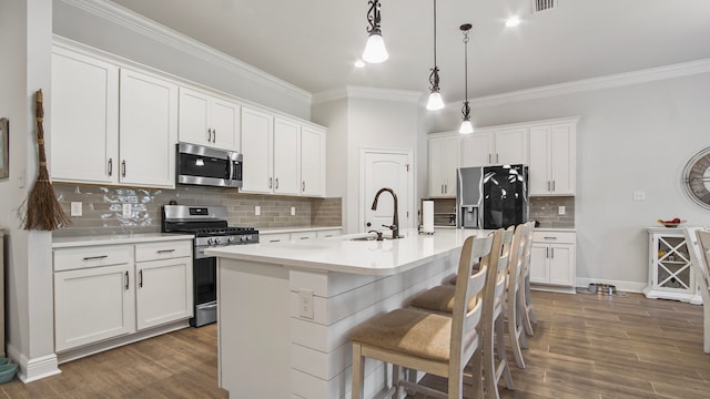 kitchen featuring dark wood-type flooring, white cabinets, hanging light fixtures, an island with sink, and appliances with stainless steel finishes