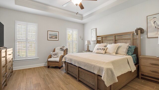 bedroom with a tray ceiling, ceiling fan, ornamental molding, and light wood-type flooring