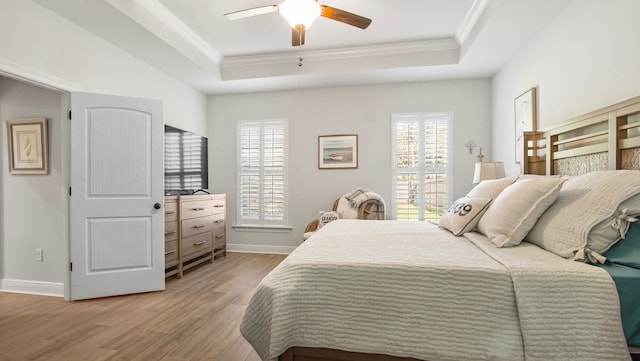 bedroom featuring ceiling fan, light wood-type flooring, a tray ceiling, and multiple windows