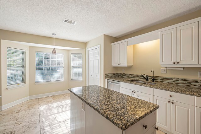 kitchen featuring white cabinetry, stainless steel dishwasher, dark stone countertops, a textured ceiling, and decorative light fixtures