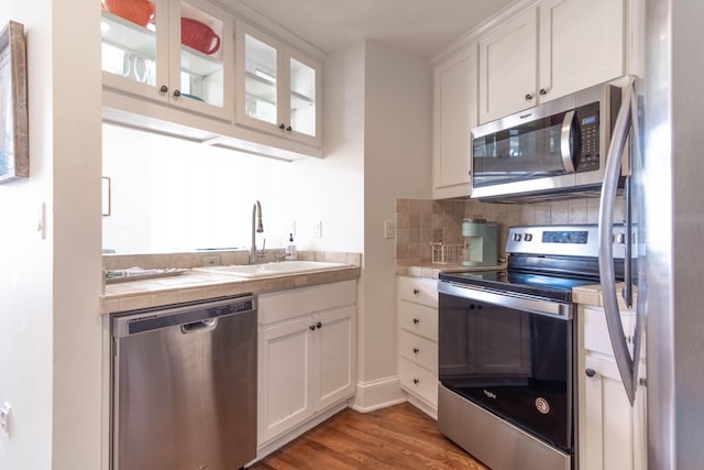 kitchen with stainless steel appliances, a healthy amount of sunlight, sink, wood-type flooring, and white cabinetry