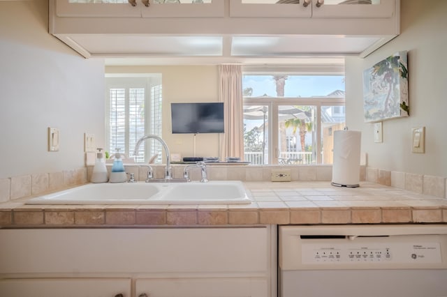 kitchen with tile counters, white dishwasher, and sink