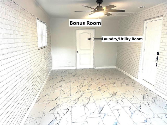 unfurnished room featuring ceiling fan and brick wall