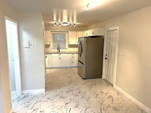 kitchen with stainless steel fridge, sink, white cabinets, and rail lighting