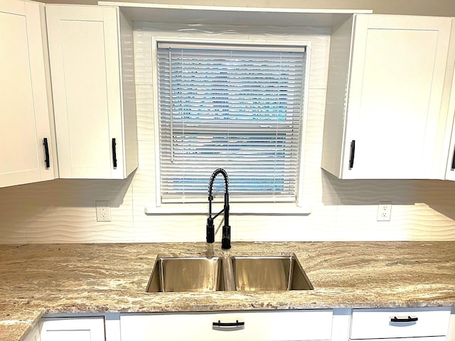 room details with white cabinets, light stone countertops, and sink