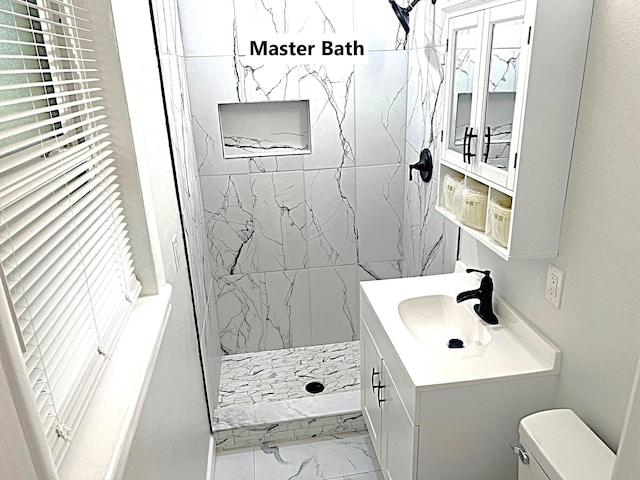 bathroom featuring a tile shower, vanity, and toilet