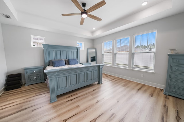 bedroom with ceiling fan, light hardwood / wood-style flooring, and a tray ceiling