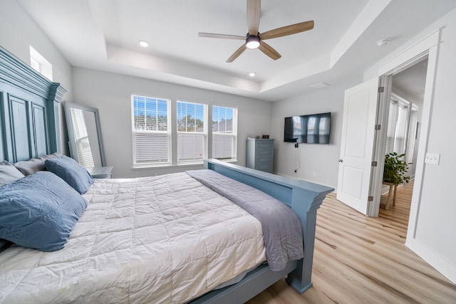 bedroom with light hardwood / wood-style flooring, ceiling fan, and a tray ceiling