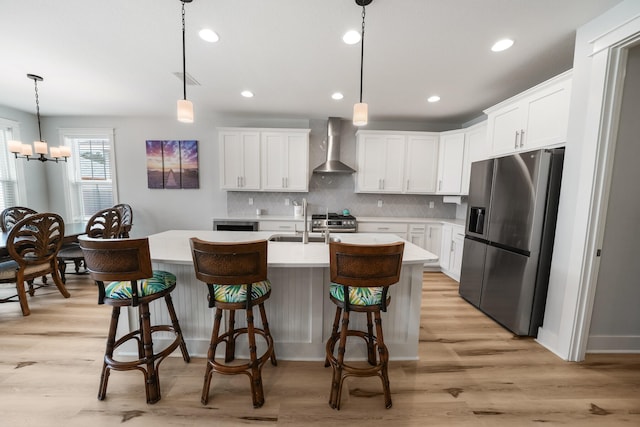 kitchen with stainless steel appliances, light hardwood / wood-style floors, wall chimney exhaust hood, hanging light fixtures, and white cabinetry