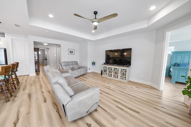 living room with ceiling fan, light hardwood / wood-style flooring, and a tray ceiling