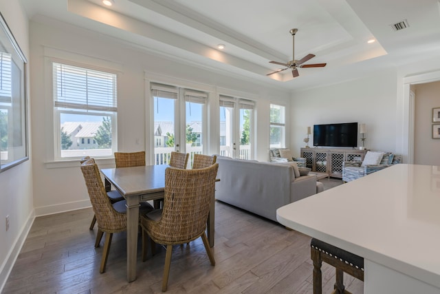 dining space with a wealth of natural light, wood-type flooring, a raised ceiling, and french doors