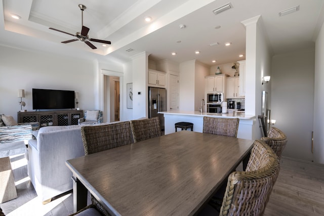 dining room with sink, ceiling fan, a raised ceiling, crown molding, and dark wood-type flooring